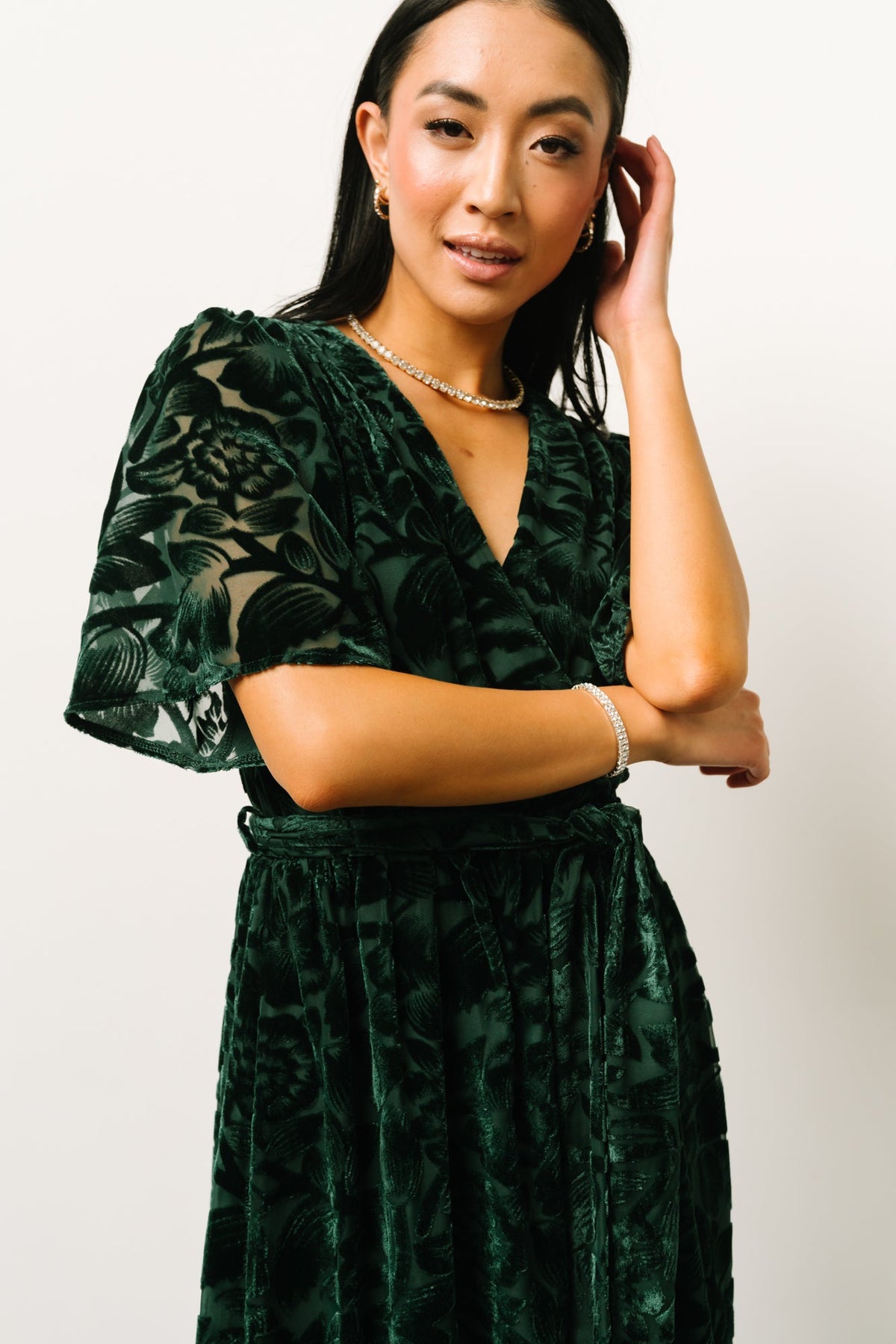 Three-quarter angled shot of dark green velvet dress showing flowy short sleeves, textured burnout floral print, and the skirt's side leg slit in motion.