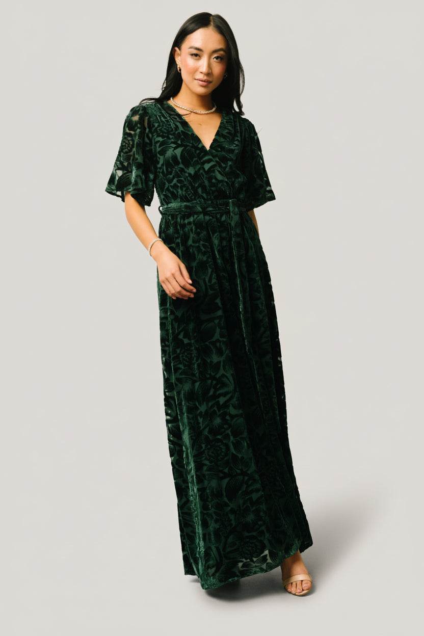 Front view of dark green Uma velvet maxi dress with burnout floral overlay, crossover surplice neckline, elastic waist, and detachable self-tie sash.